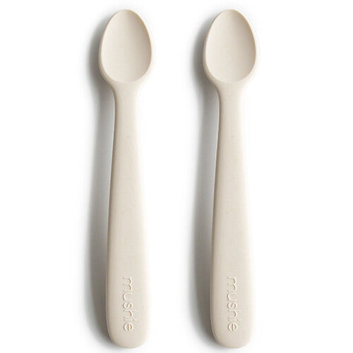 Twee mushie siliconen babylepels in ivoorkleur op een witte achtergrond.