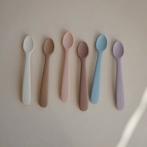 Zes mushie siliconen babylepels in verschillende pastelkleuren.