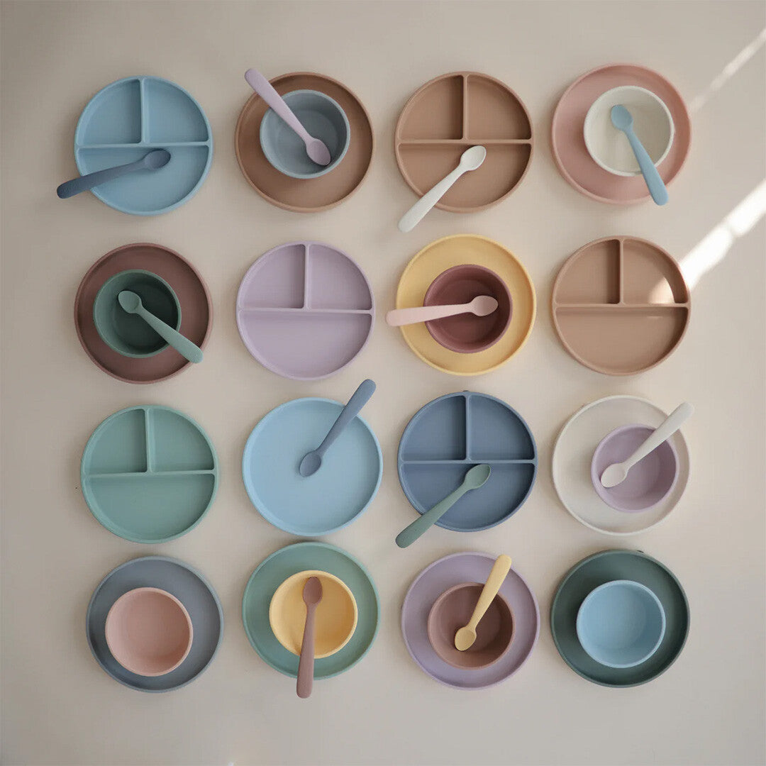 Overzicht van mushie siliconen babyvoedingssets met verdeelde borden, kommen en lepels in diverse pastelkleuren.