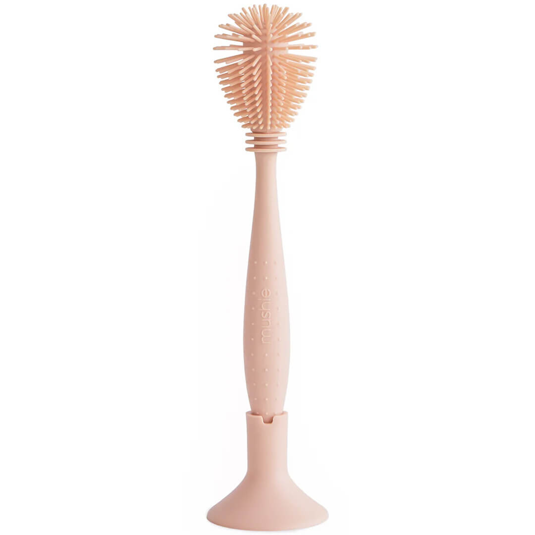 Mushie siliconen flessenborstel in blush kleur, staand op een witte achtergrond.
