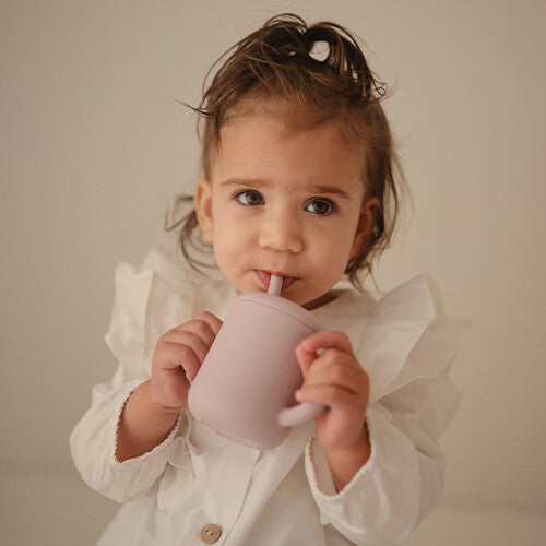 Een peuter drinkt uit een zacht lila siliconen kinderbeker met rietje.