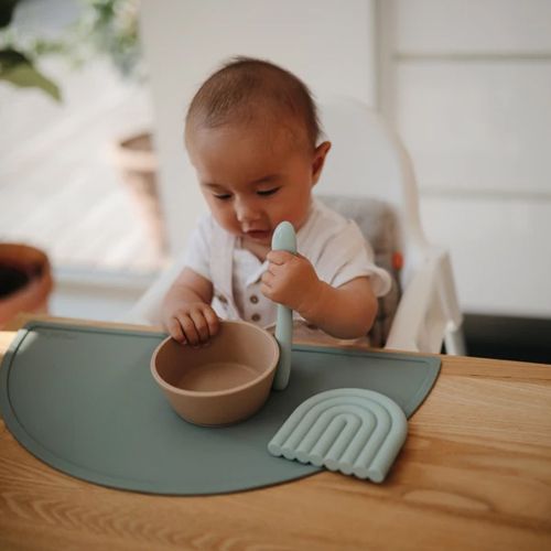 Een baby zit aan tafel met een Mushie siliconen kinderkom, lepel en placemat.