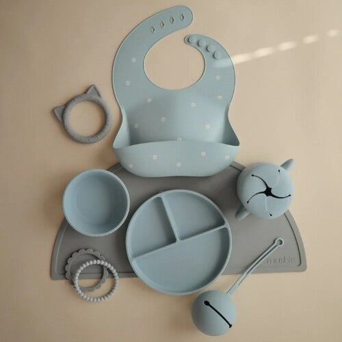 Mushie siliconen babyvoedingsset in poederblauw en grijs, met slab, kom, bord en speelgoed.