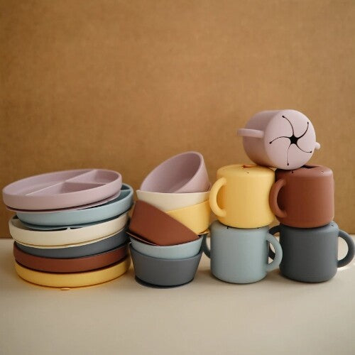 Gestapelde mushie siliconen babyvoedingsartikelen in diverse pastelkleuren, waaronder borden, kommen, snackcups en bekers.