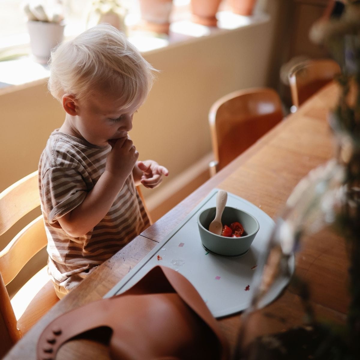 Een blond kindje eet aan tafel uit een groen kommetje met een mushie siliconen lepel.