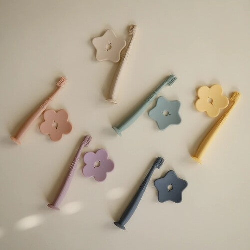 Zes mushie siliconen kindertandenborstels in pastelkleuren met stervormige houders.