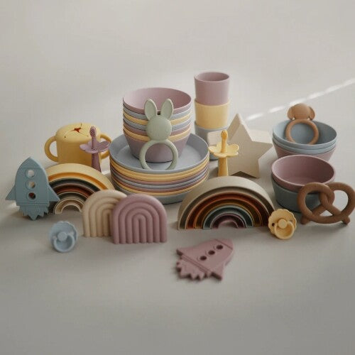 Een collectie mushie siliconen babyproducten in pastelkleuren, waaronder servies, bijtringen en stapelbare regenboogjes.