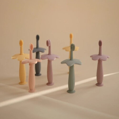 Zeven mushie siliconen kindertandenborstels in diverse pastelkleuren met bloemvormige bescherming.