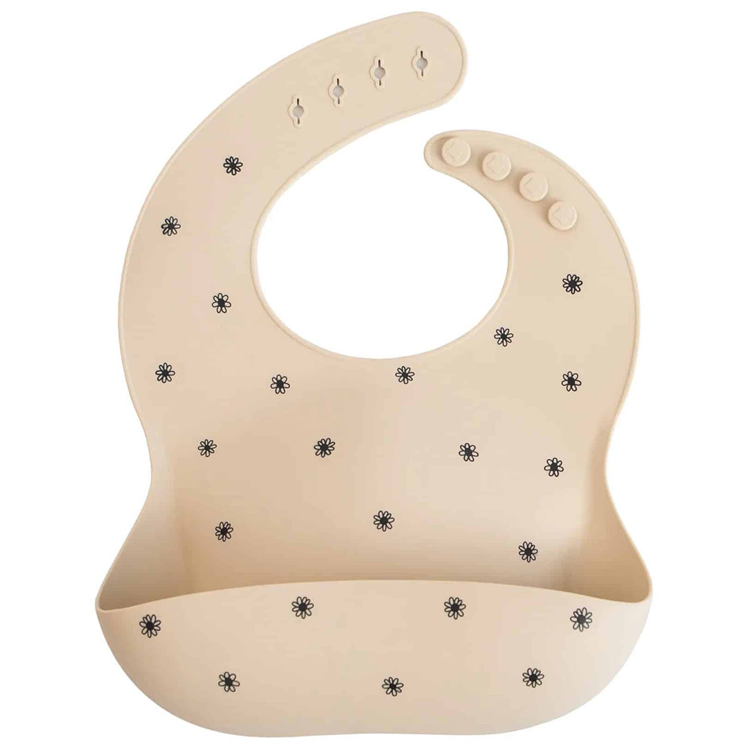 Mushie siliconen babyslab in beige met zwart madeliefjespatroon.
