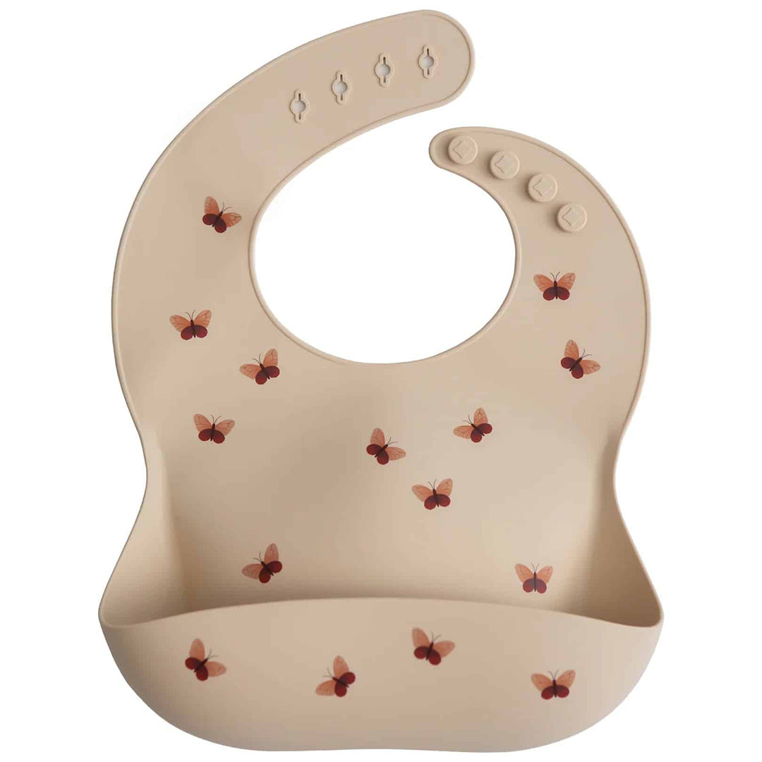 Mushie siliconen slabbetje voor babyvoeding in beige met vlinderpatroon.