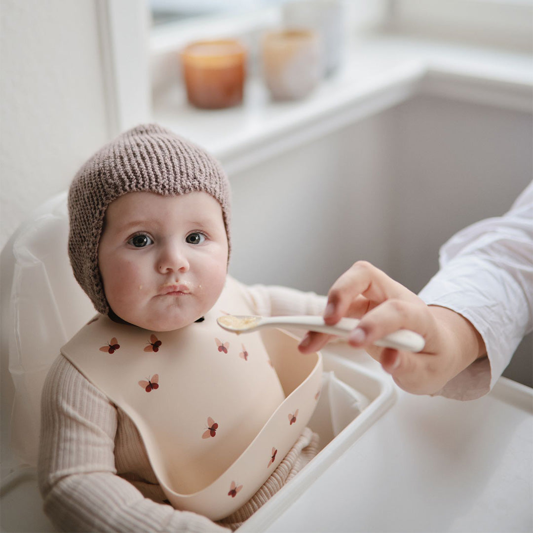 Een baby draagt het mushie siliconen slabbetje met vlinders terwijl het gevoed wordt.
