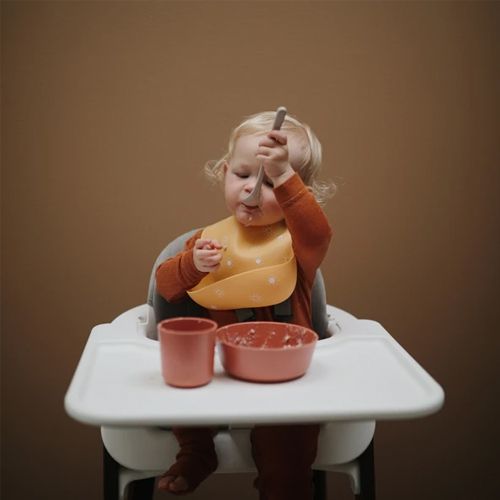 Een baby met een mushie siliconen slabbetje eet zelfstandig in een kinderstoel.