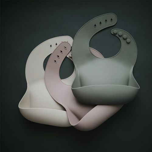 Drie mushie siliconen slabbetjes in beige, roze en groen liggen over elkaar.