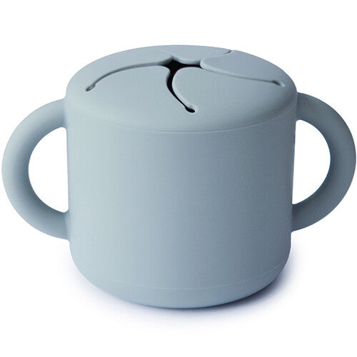 Mushie siliconen snackbeker in lichtblauw met twee handvatten en een deksel met stervormige opening op een witte achtergrond.
