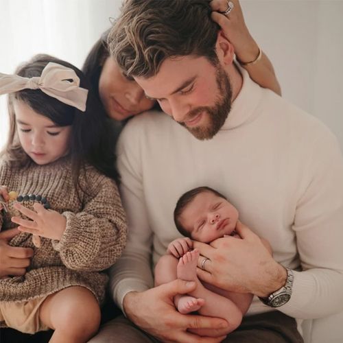 Een familieportret met een vader die een pasgeboren baby vasthoudt, naast een moeder en een jong meisje.