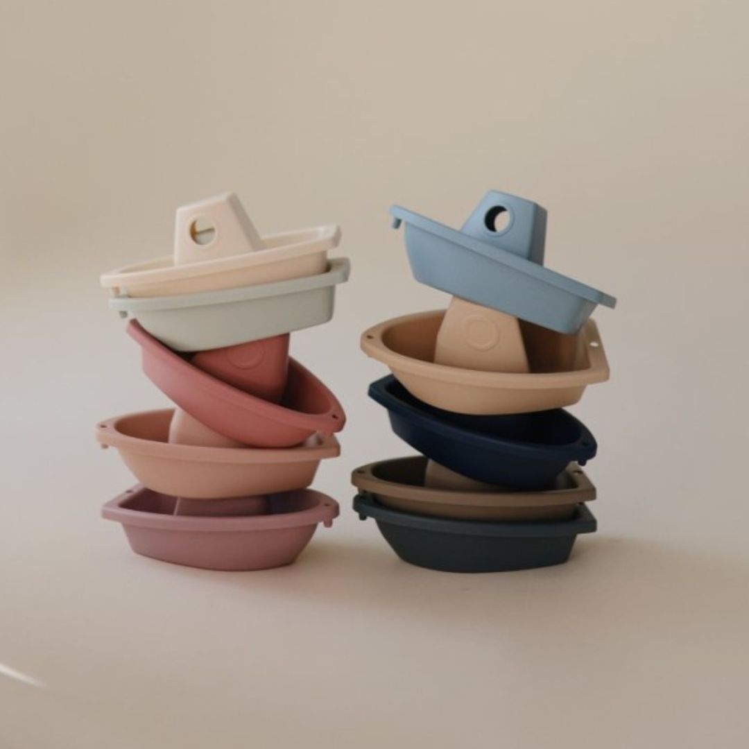 Twee stapels Mushie badbootjes in verschillende pastel- en aardetinten.