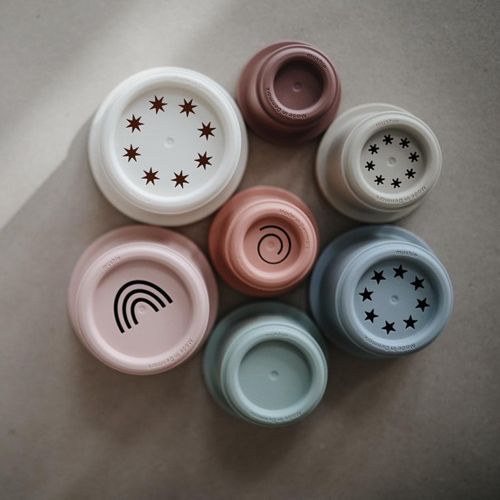 mushie stapelbekers van bovenaf gezien, gerangschikt in een cirkel, met patronen zoals sterren en een regenboog op de bodems.