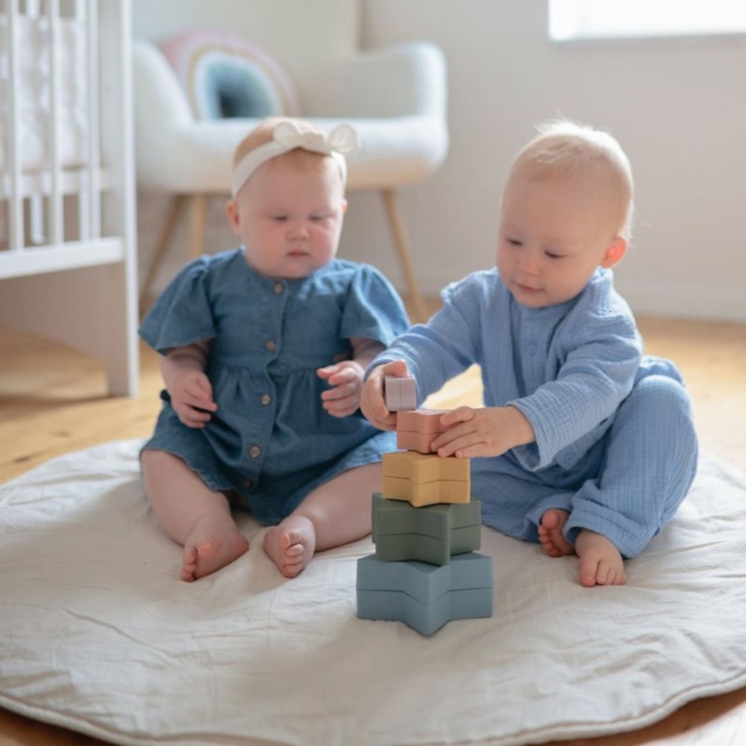 Twee baby's spelen met de mushie stapeltoren van veelkleurige sterren.