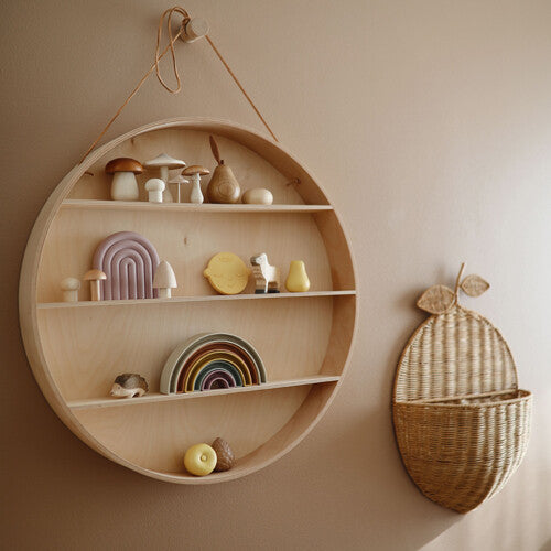 De mushie regenboog stapeltoren staat als decoratie op een ronde houten wandplank.