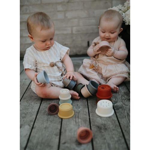 Twee baby's spelen buiten op een houten vlonder met de mushie stapelbekers.