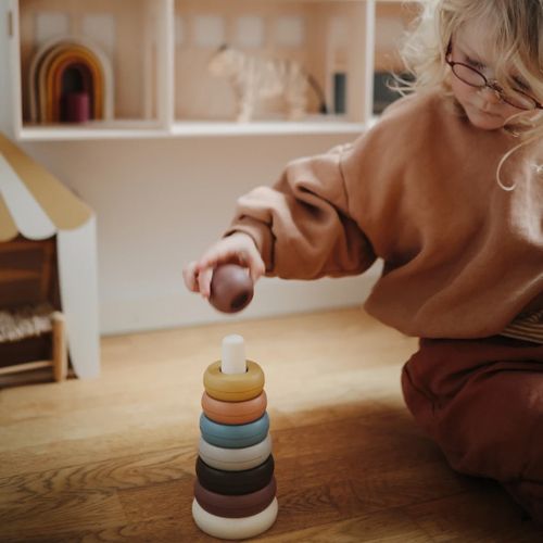 Een kind speelt met de Mushie stapeltoren op een houten vloer.