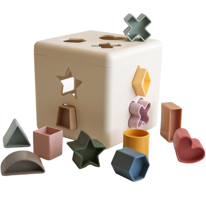 Beige mushie vormendoos met diverse gekleurde geometrische vormen eromheen en deels erin.