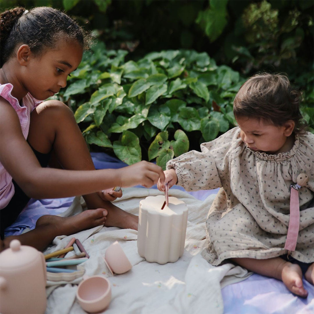 Twee kinderen spelen buiten met de vormenstoof, waarbij een staafje in de beige container wordt gestoken.