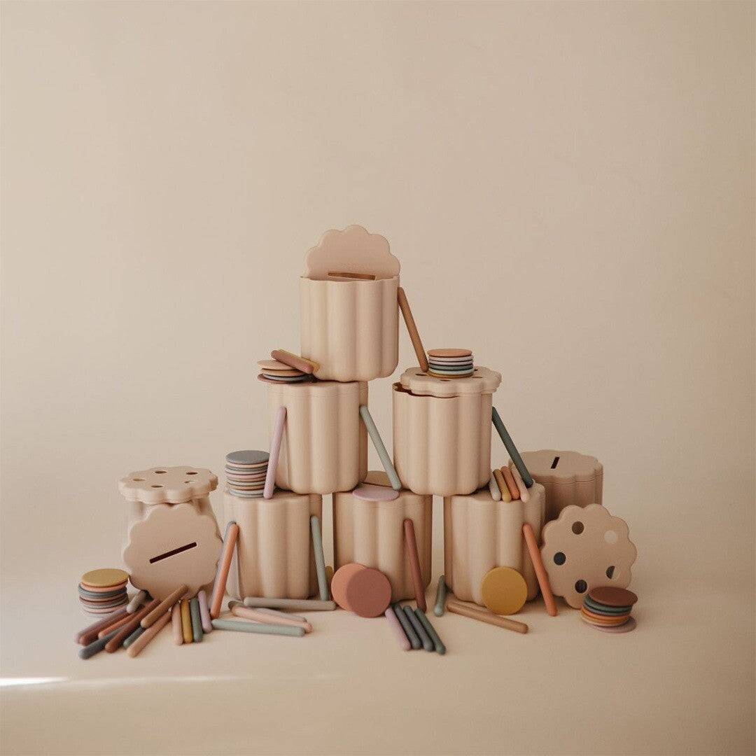 Een collectie van meerdere mushie vormenstoof sets met beige containers en diverse pastelkleurige munten en staafjes.