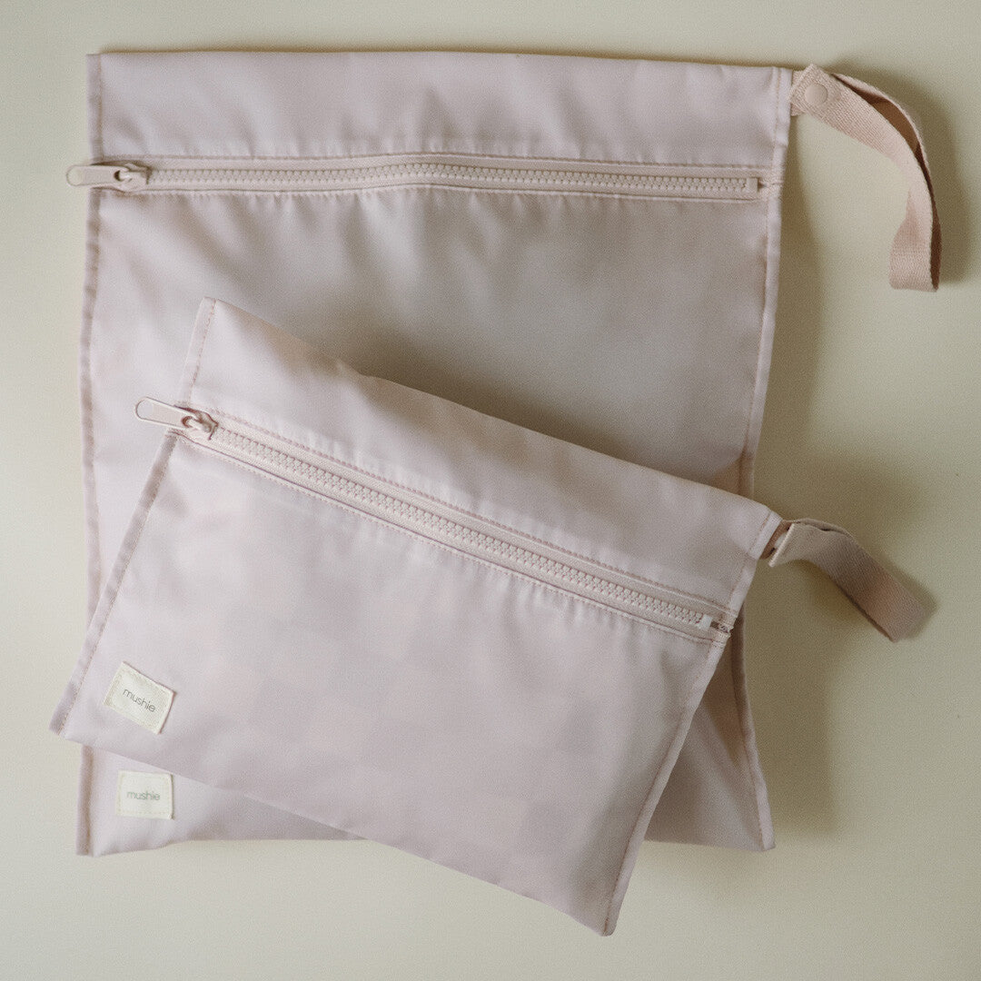 Bovenaanzicht van twee roze Mushie waterproof opbergzakken met ritsen en lussen op een lichte ondergrond.