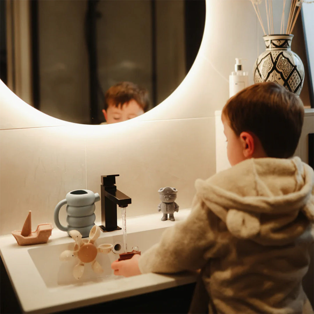 Een kind speelt met Mushie piraten badspeeltjes in een wasbak in de badkamer.