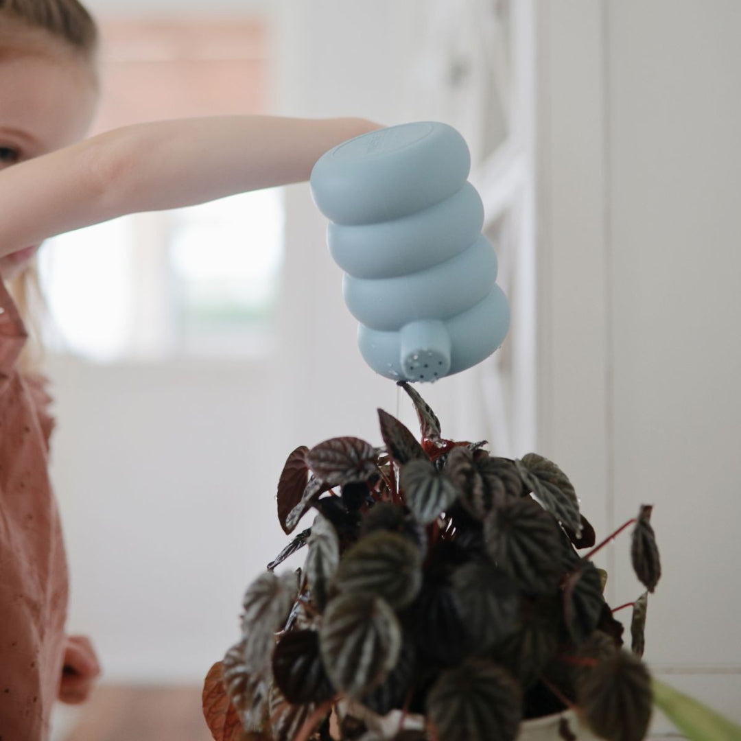 Een kind giet water met de mushie siliconen gieter op een plant.
