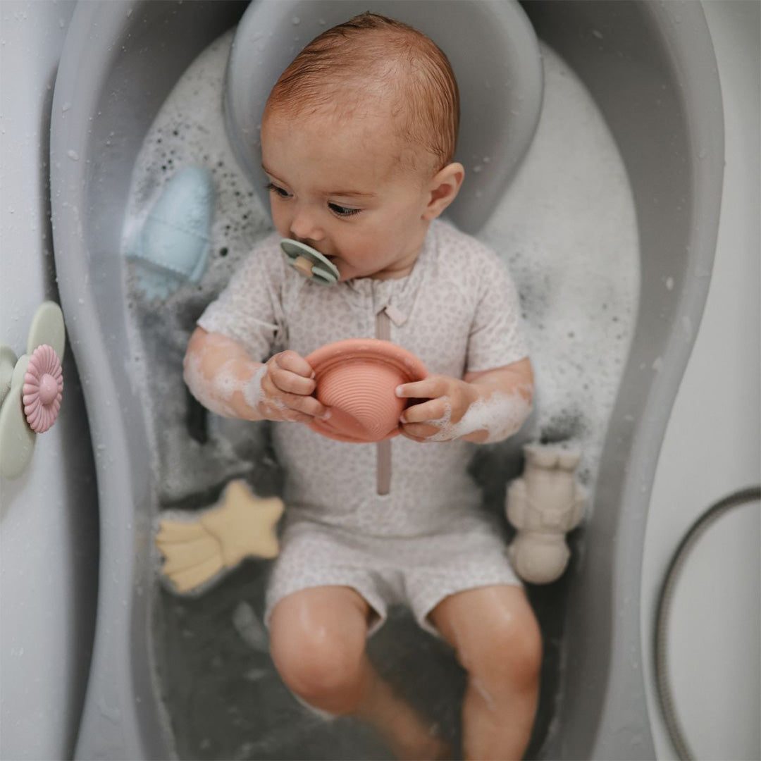 Een baby in bad speelt met een Mushie siliconen speelgoedset in astronautenthema.