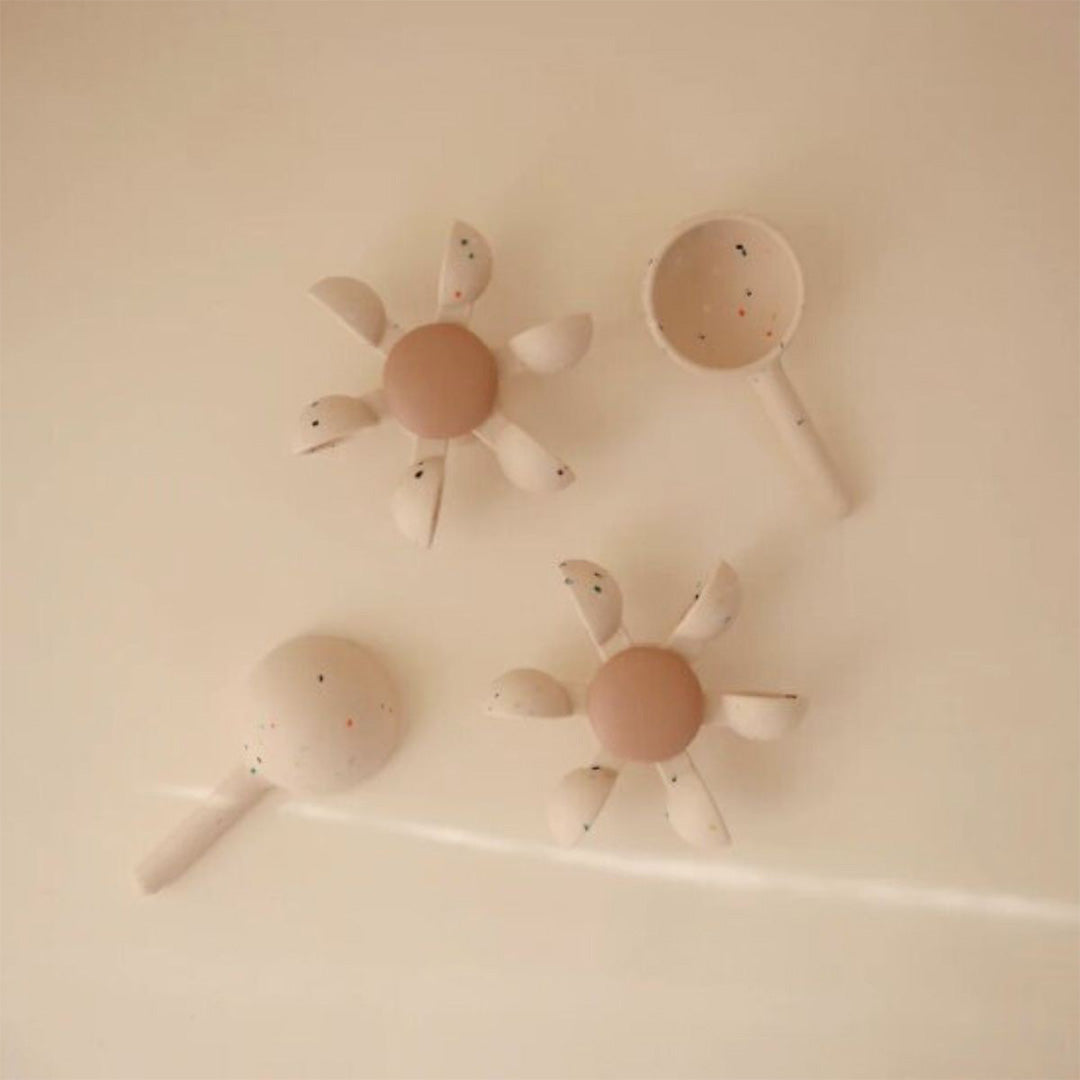 Drie Mushie siliconen babyspeeltjes met spikkels, waaronder twee bolvormige en een schepje, drijven in water.