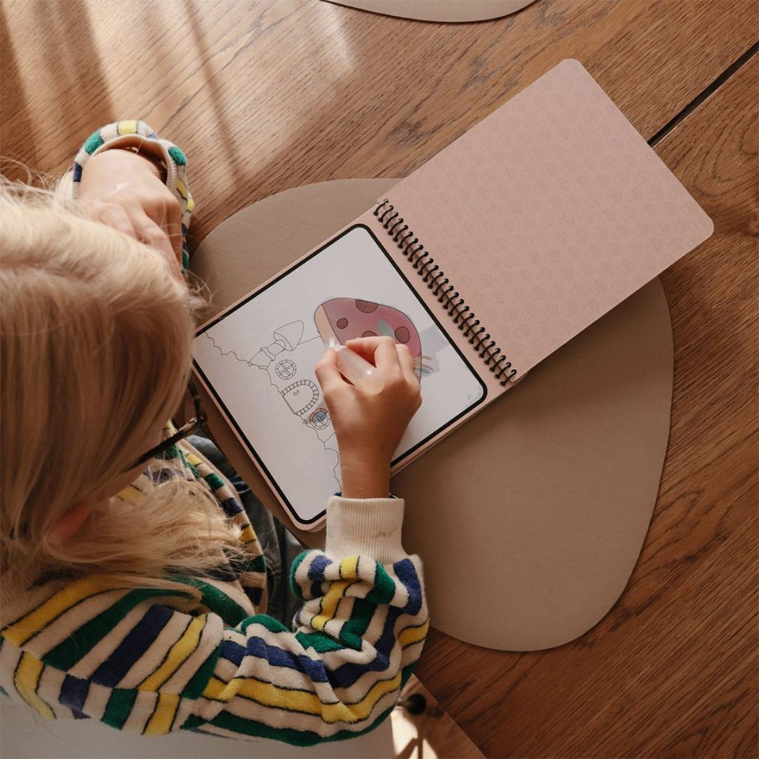 Een kind kleurt een paddenstoel in een Mushie herbruikbaar waterkleurboek met een waterpen.