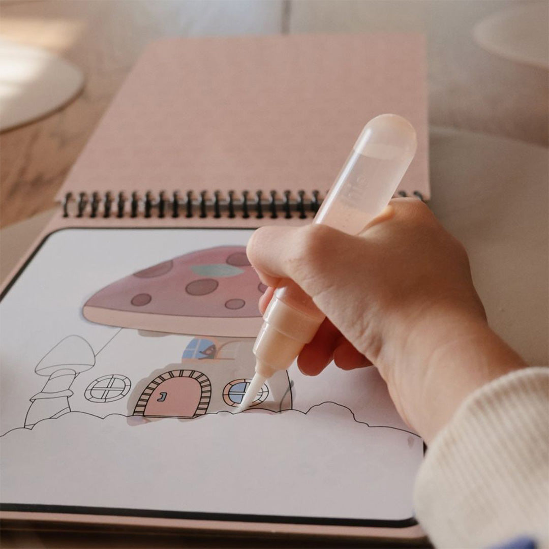 Detail van een hand die een paddenstoelhuisje kleurt in een Mushie herbruikbaar waterkleurboek.
