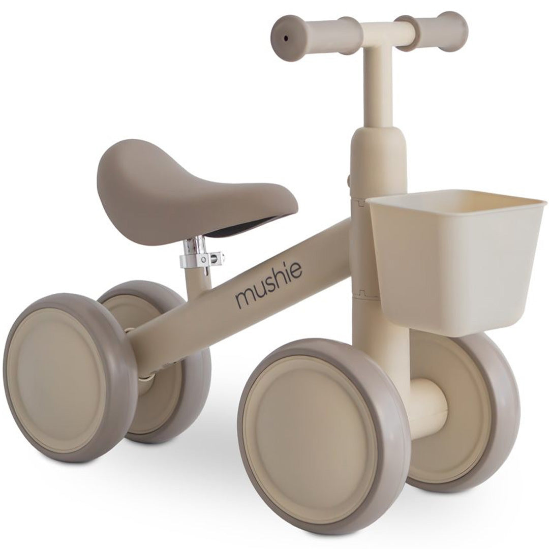 Mushie loopfiets in shifting sand kleur met vier wielen en een mandje aan het stuur.