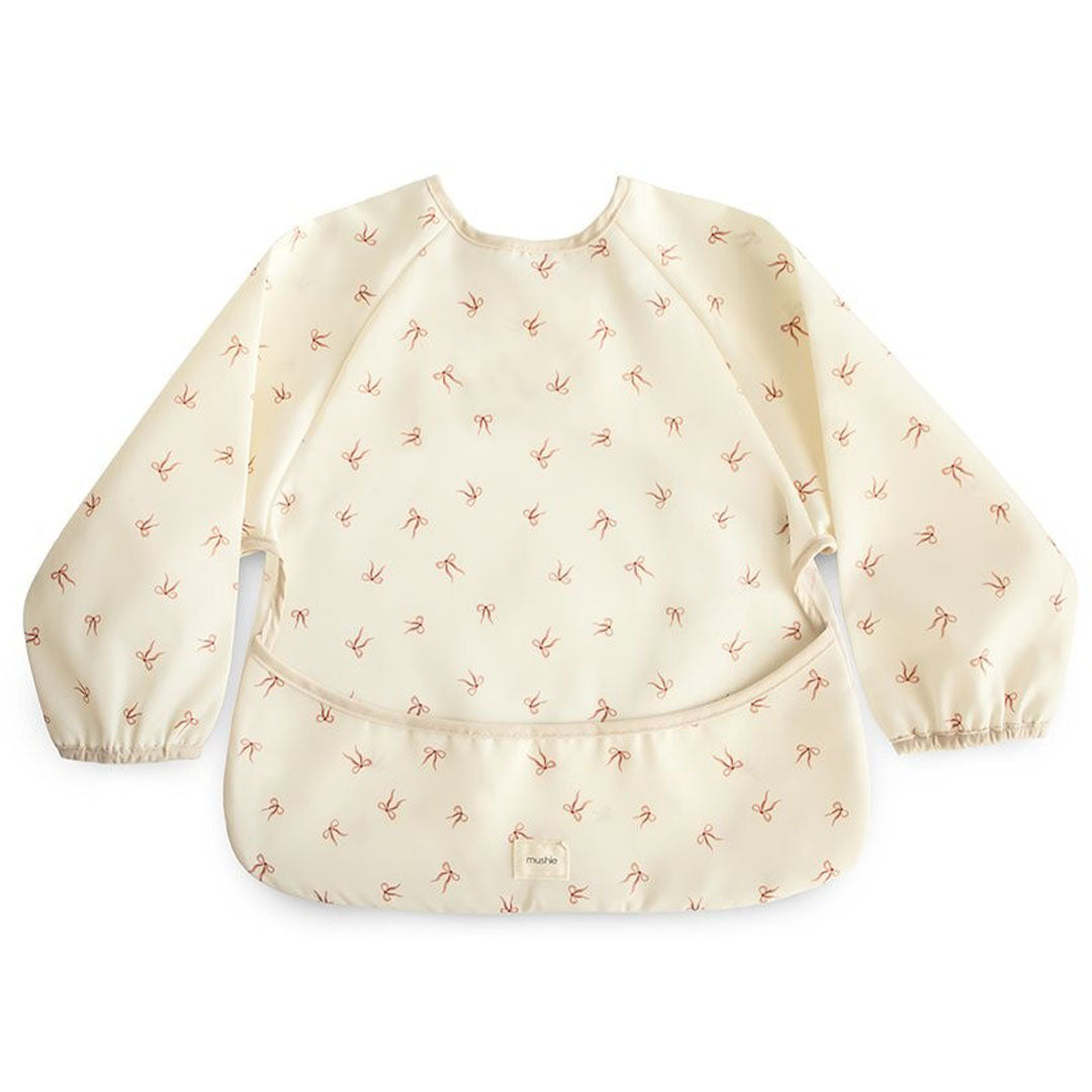 Mushie mouwslab voor baby's in beige met een patroon van rode strikjes.