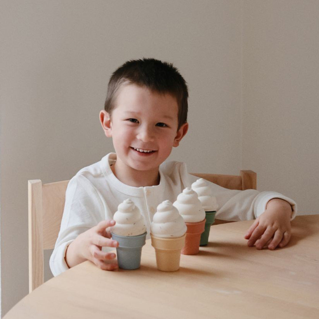 Een lachende jongen speelt aan tafel met mushie siliconen ijsjes speelgoed.