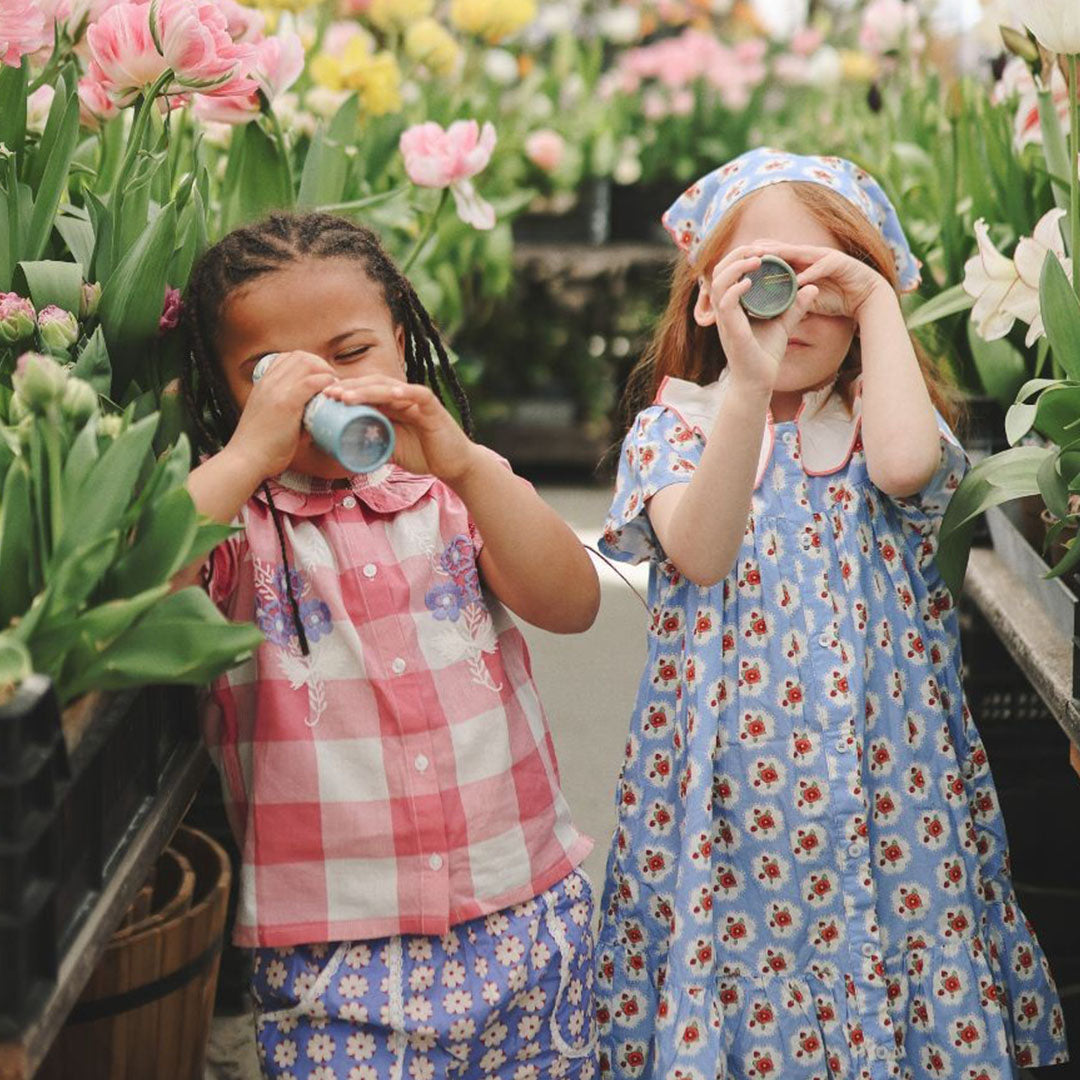 Twee meisjes kijken door kaleidoscopen in een bloementuin.