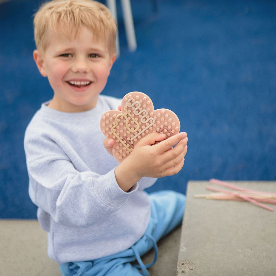 Een lachende jongen houdt een roze bloemvormig sensorisch speeltje met nopjes vast.