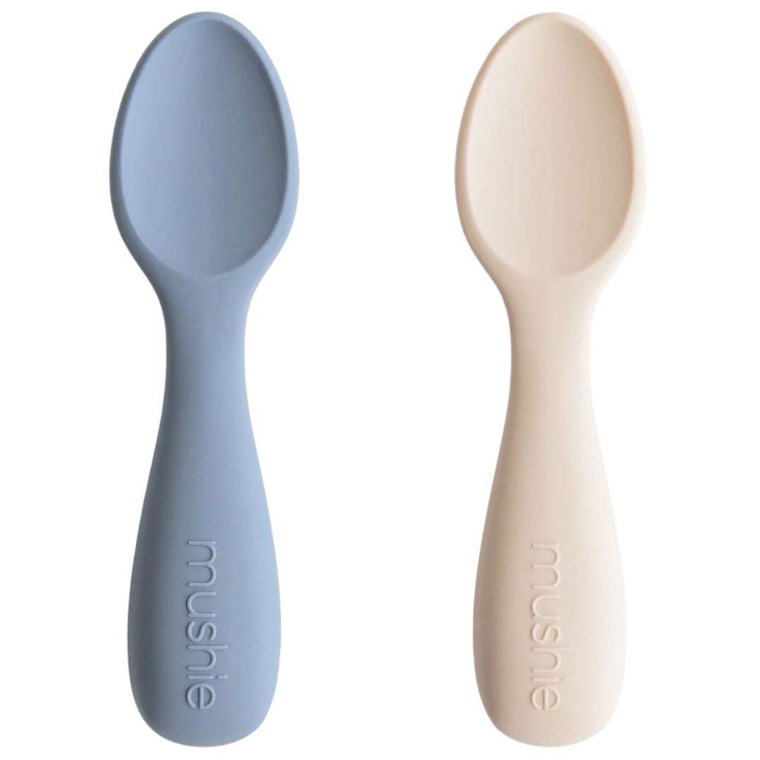 Twee Mushie siliconen kinderlepels, één blauw en één beige.