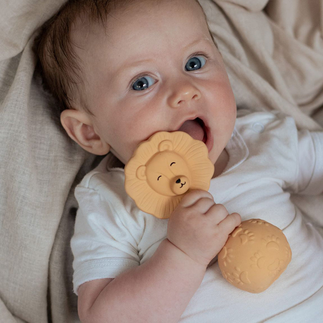 Een baby met blauwe ogen bijt op het natruba leeuw bijtspeelgoed met rammelaar.