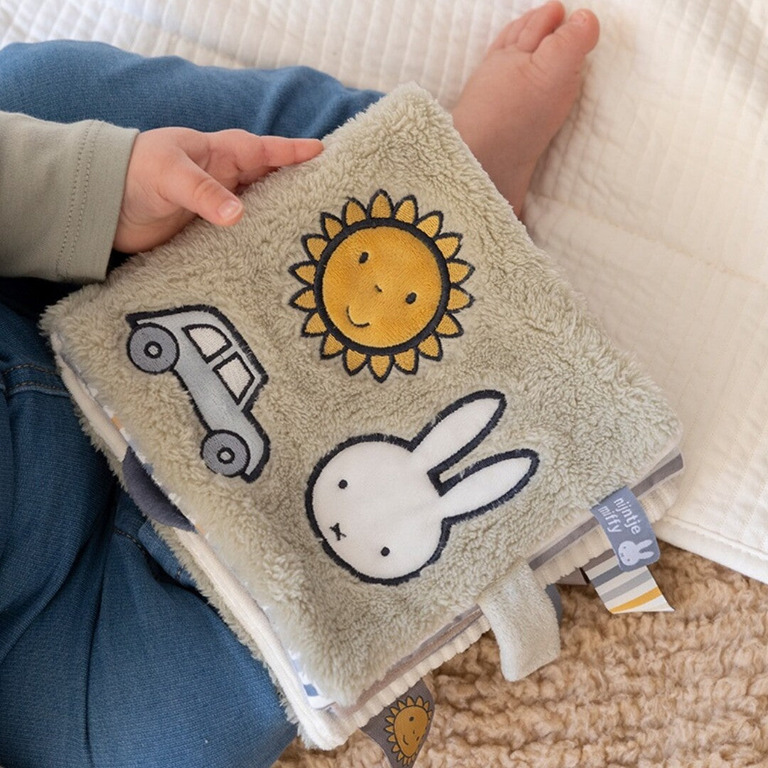 Een baby houdt het Nijntje-miffy activiteitenboek vast met de beige voorkant met zon, auto en Nijntje zichtbaar.