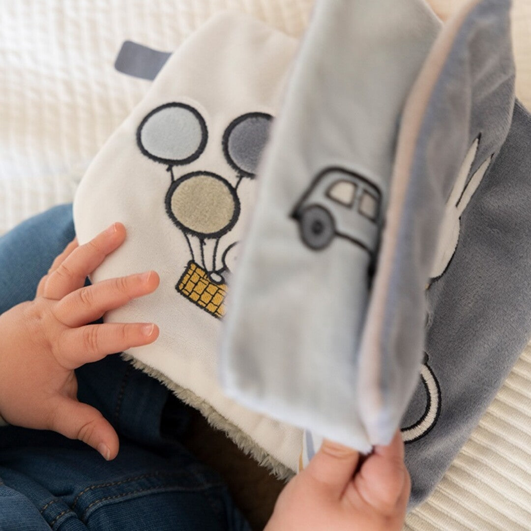 Een baby bladert door het Nijntje-miffy activiteitenboek met de pagina van Nijntje in een luchtballon zichtbaar.