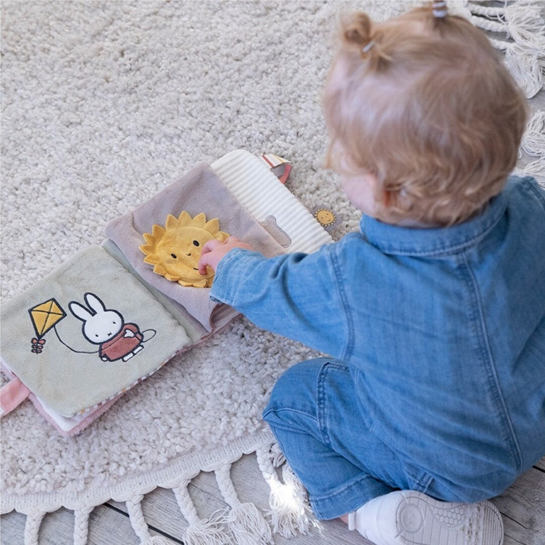 Een baby speelt op een kleed met het open Nijntje activiteitenboek voor baby's, waarop Nijntje met een vlieger en een zon te zien zijn.