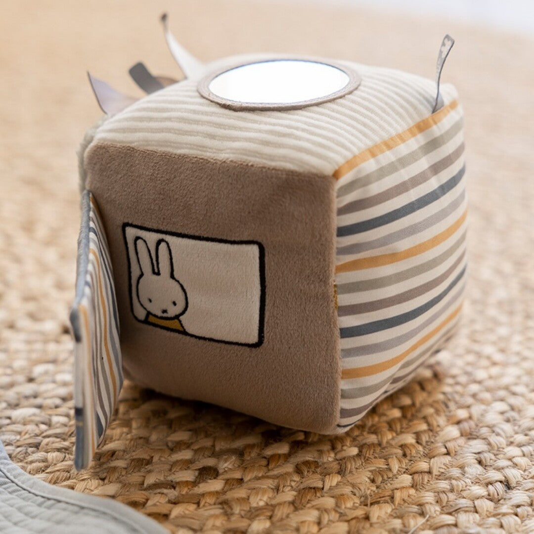 De nijntje-miffy activiteitenkubus ligt op een gevlochten mat en toont Miffy die uit een raam kijkt.