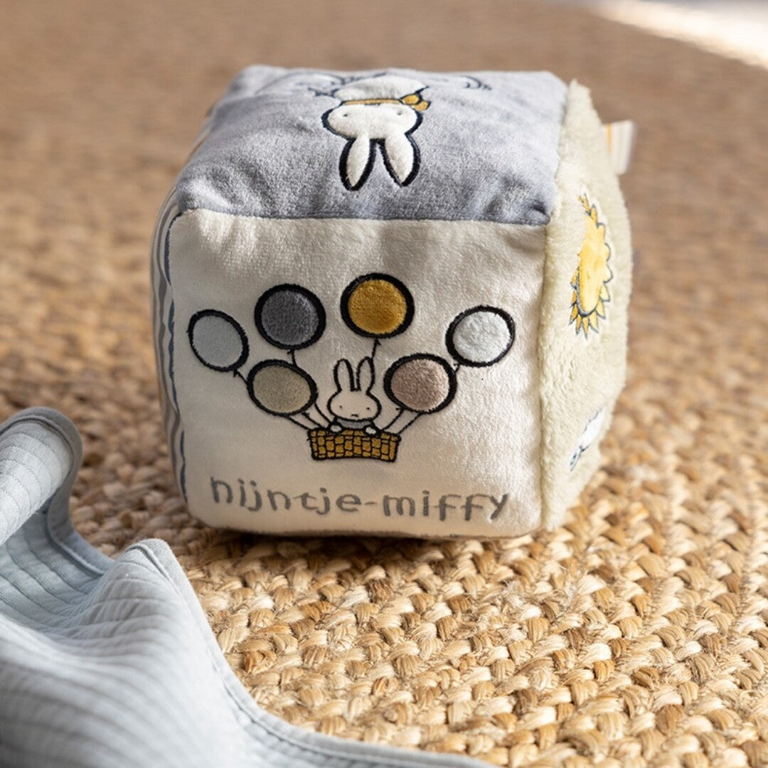 De nijntje-miffy activiteitenkubus met Miffy in een mandje met ballonnen en de merknaam op een witte zijde.