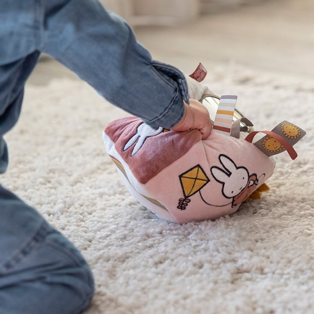Een kind speelt met de nijntje-miffy activiteitenkubus op een zacht tapijt.