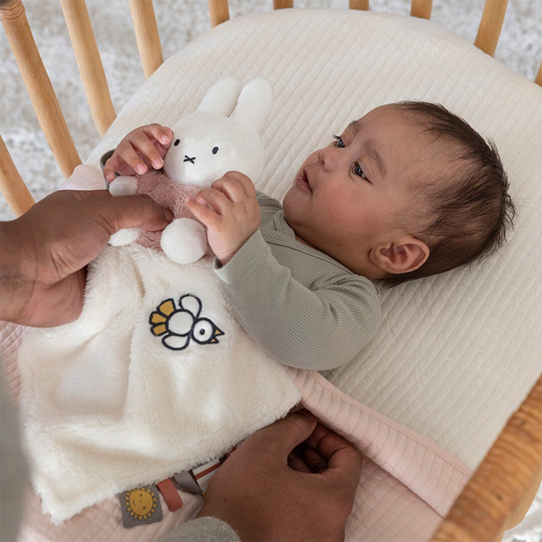 Een baby ligt in een wiegje en speelt met het Nijntje-miffy pluchen knuffeldoekje.