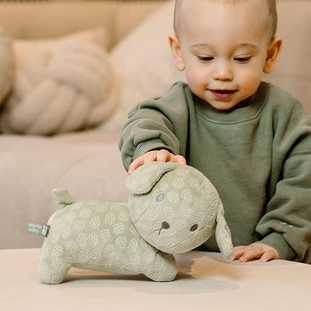 Een peuter speelt aan tafel met de groene nijntje-miffy pluchen knuffelhond Snuffie.